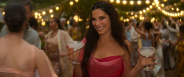 Sandra Bullock smiles holding two margaritas in a still from the movie Practical Magic 2.